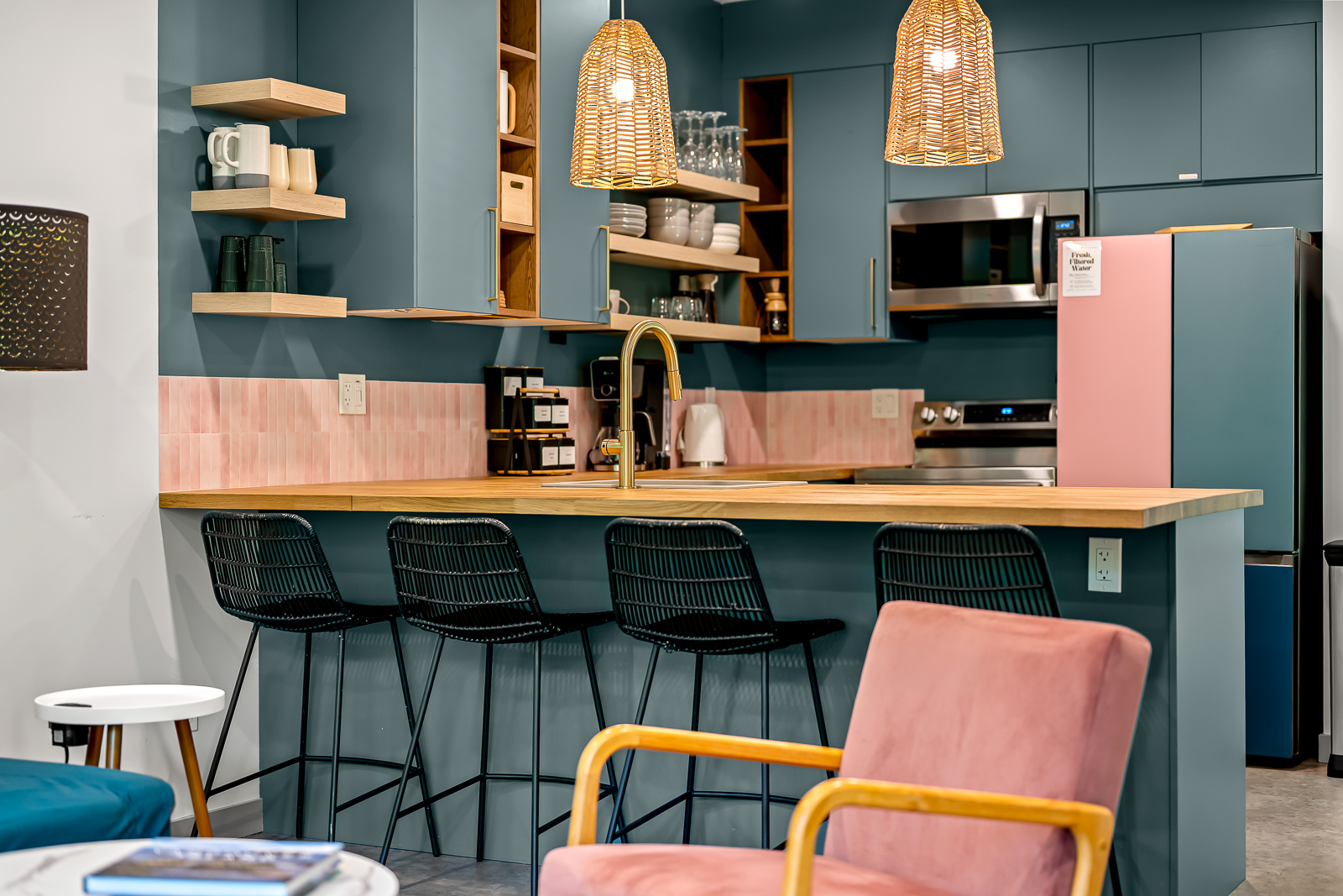 Guest house kitchen — teal cabinets, pink tile backsplash, rattan pendants, butcher block