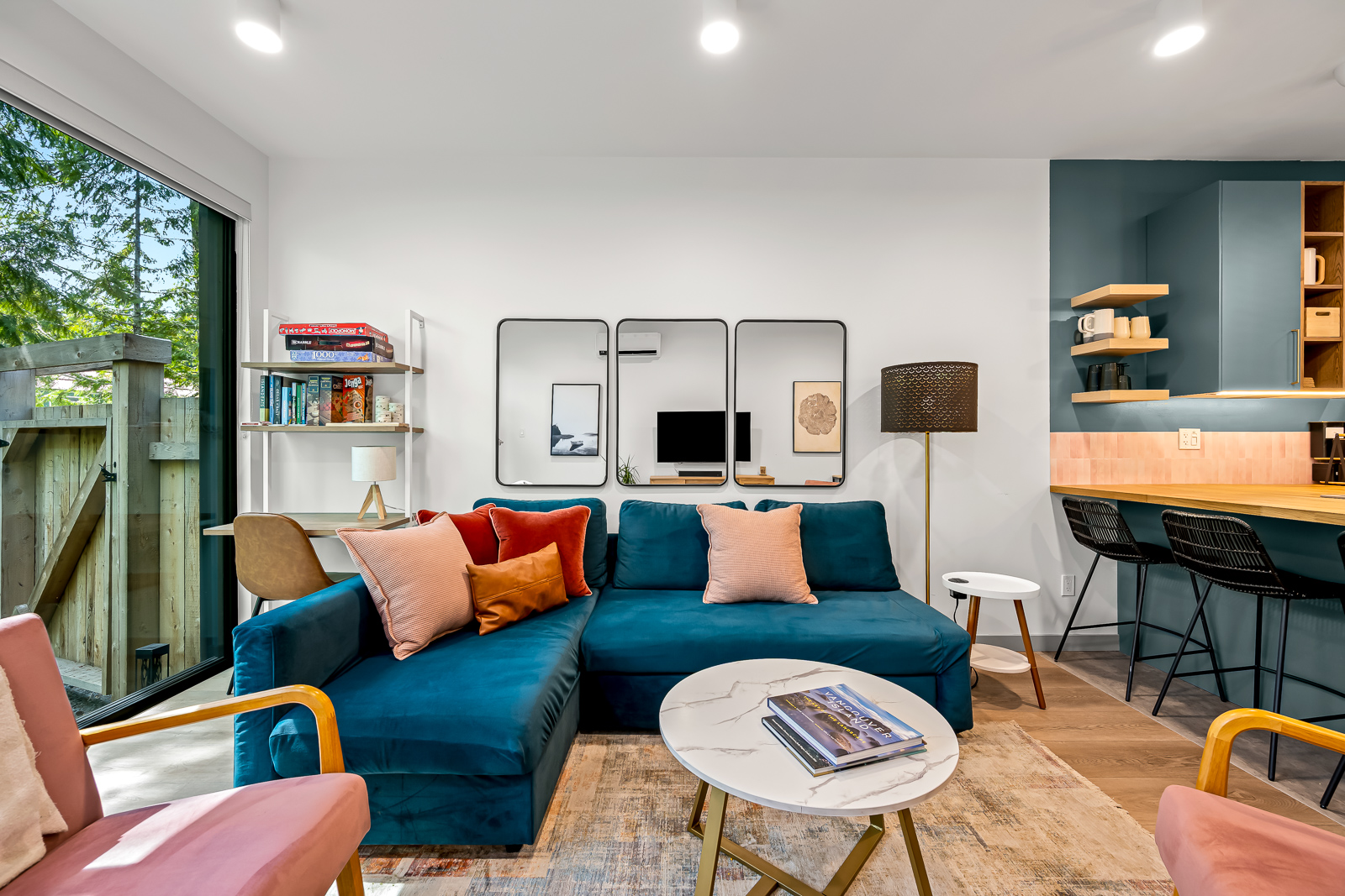Guest house living room — teal sectional, pink accent chairs, sliding doors to fenced yard