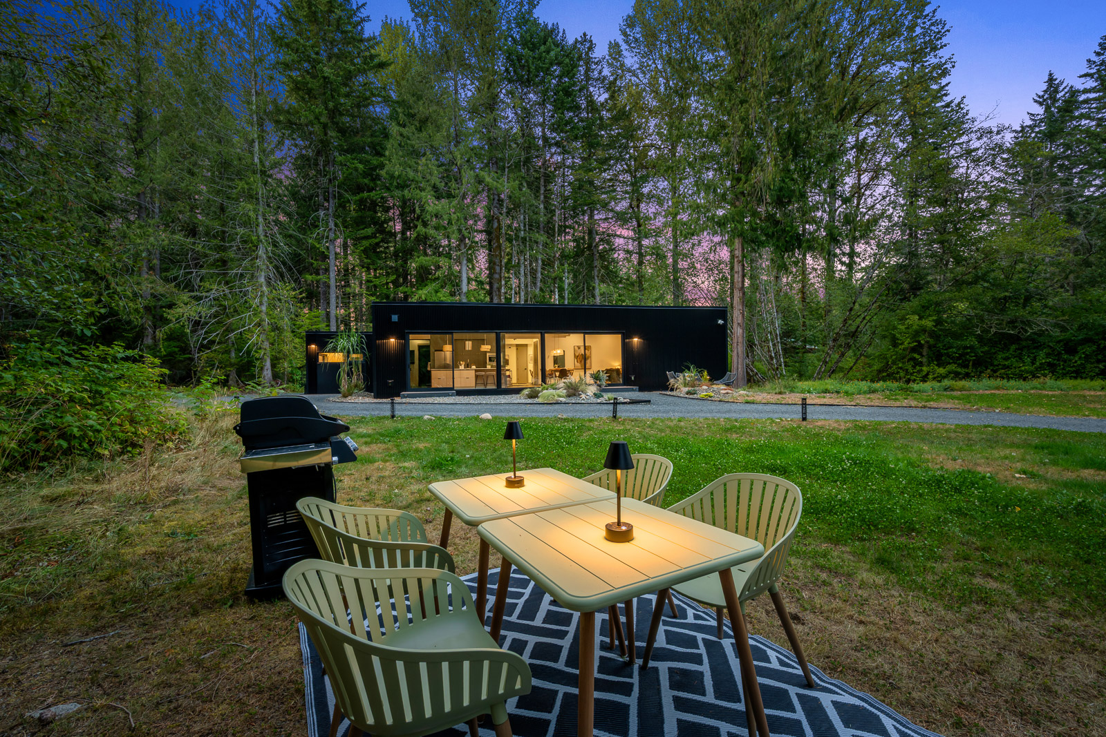 The guest house backyard at twilight with outdoor dining and warm interior glow