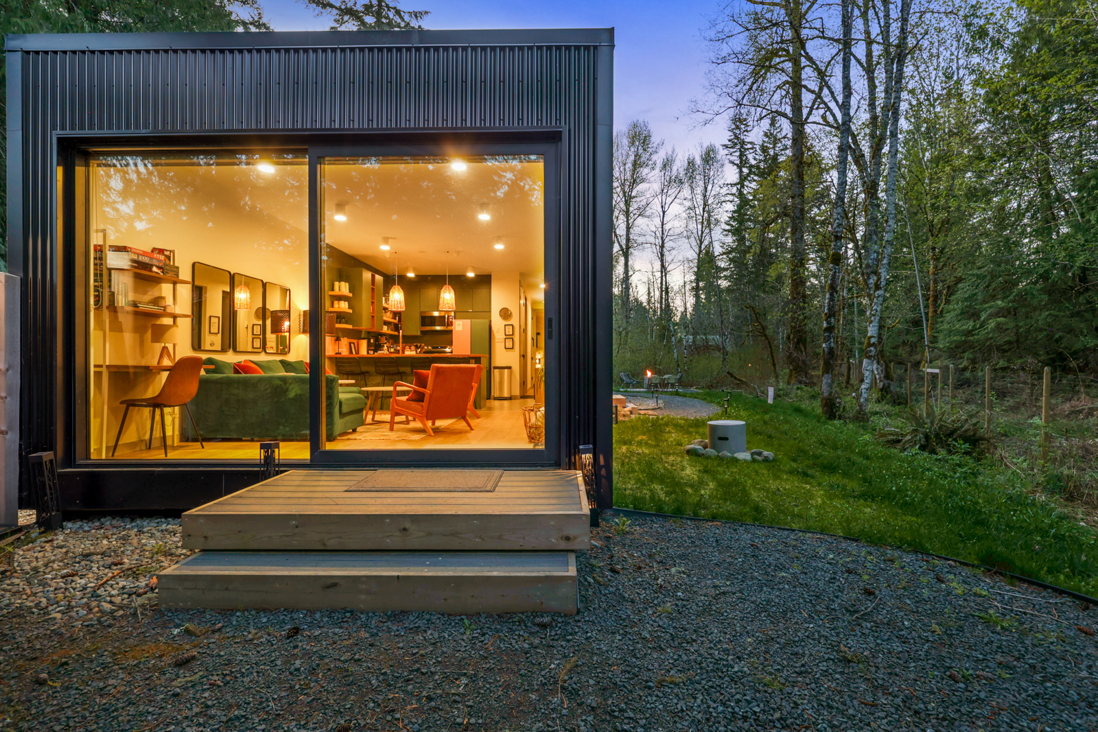 The second home glowing at dusk — full-width glass doors open to the forest