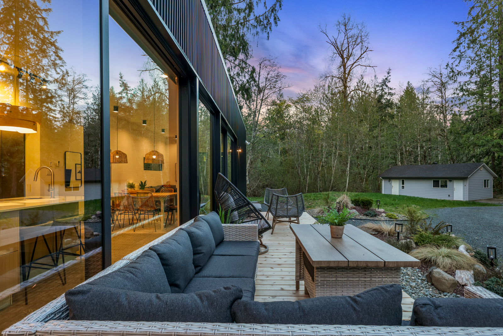 Main residence deck at dusk — sectional sofa, boardwalk, and forest under a pink sky