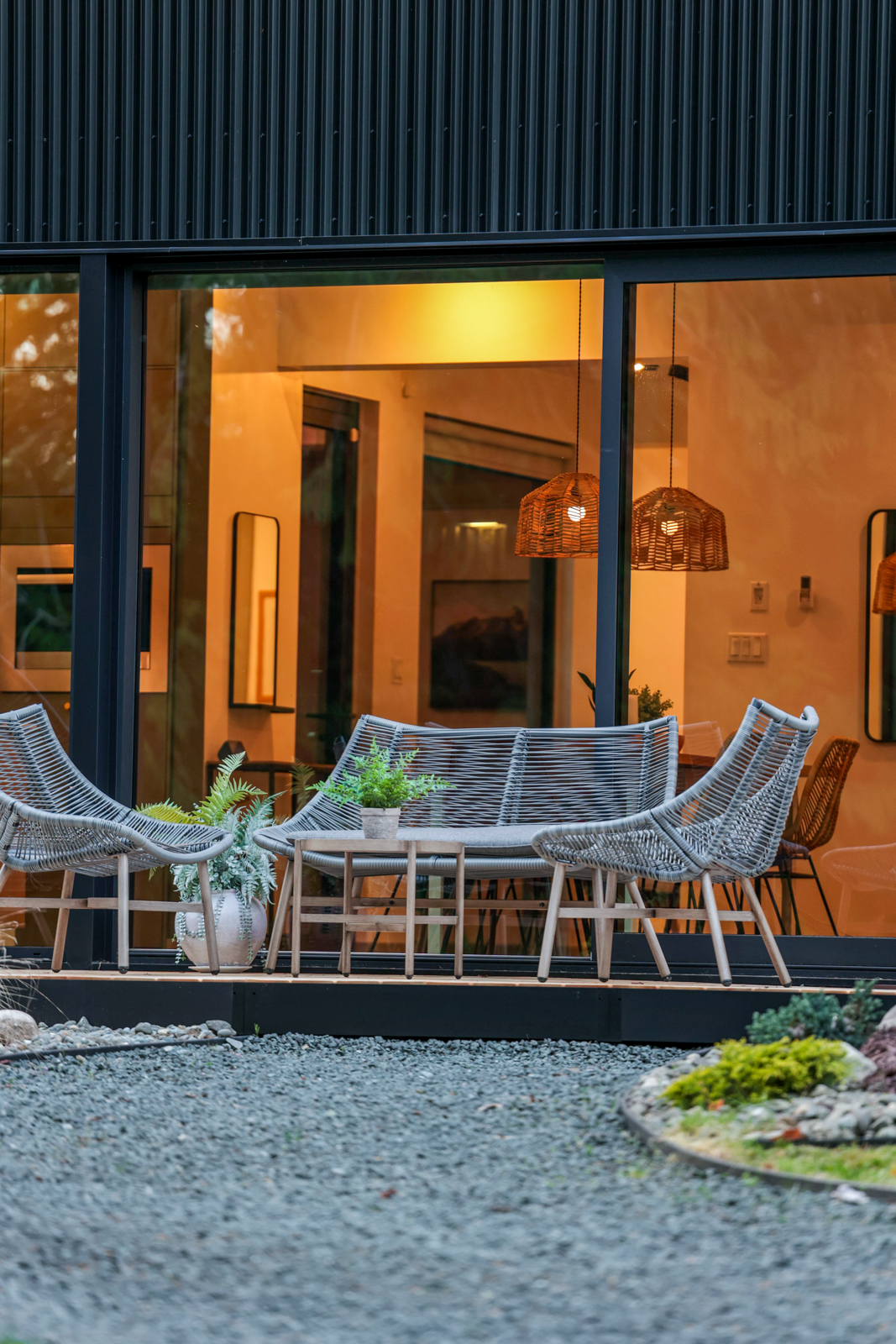 Main residence patio — woven lounge chairs in the evening light, warm glow through the glass wall behind