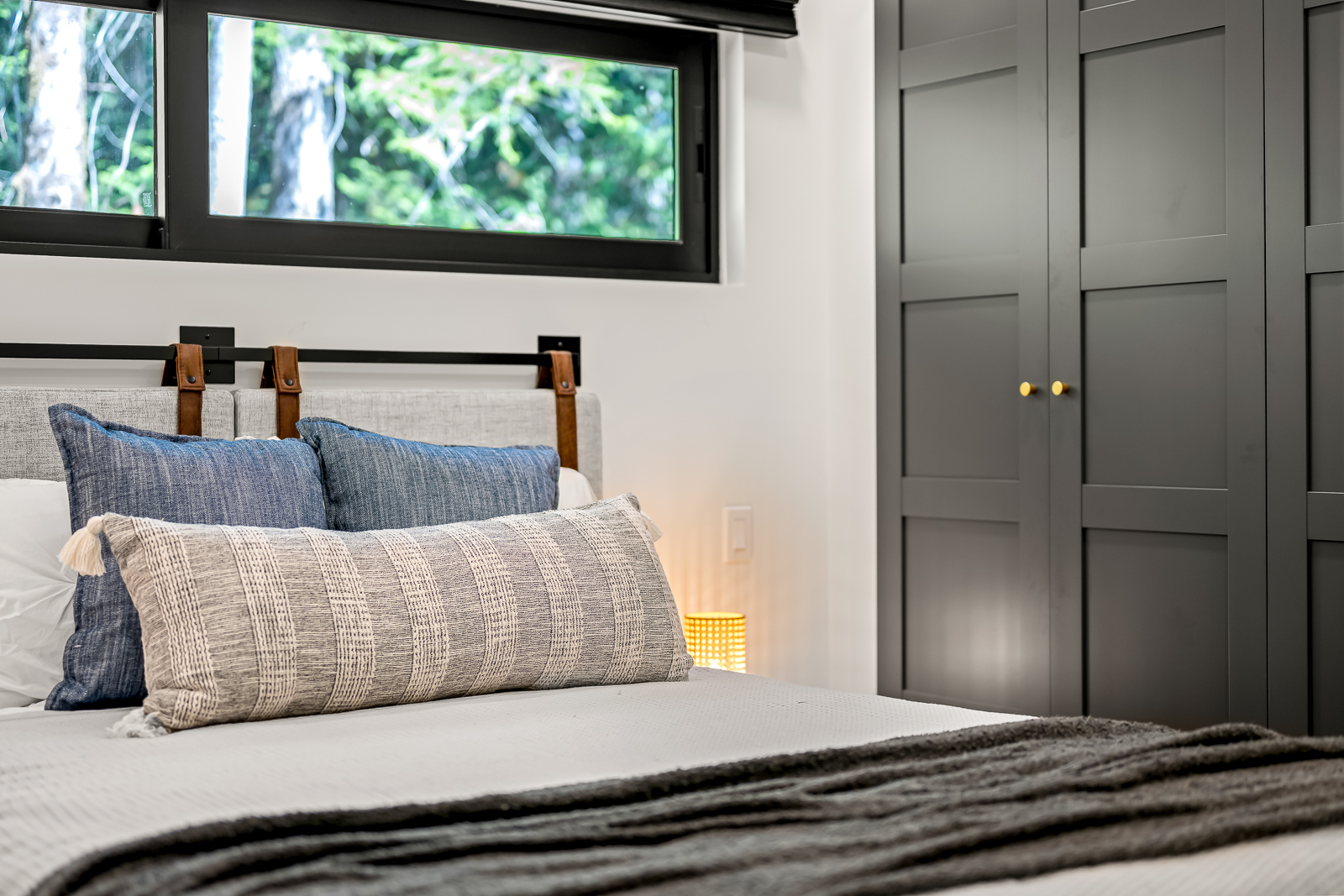 Second bedroom with leather-strap headboard, clerestory windows, and forest light