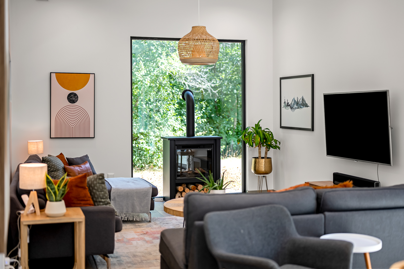 Living area with wood stove, tall window to forest, and comfortable seating